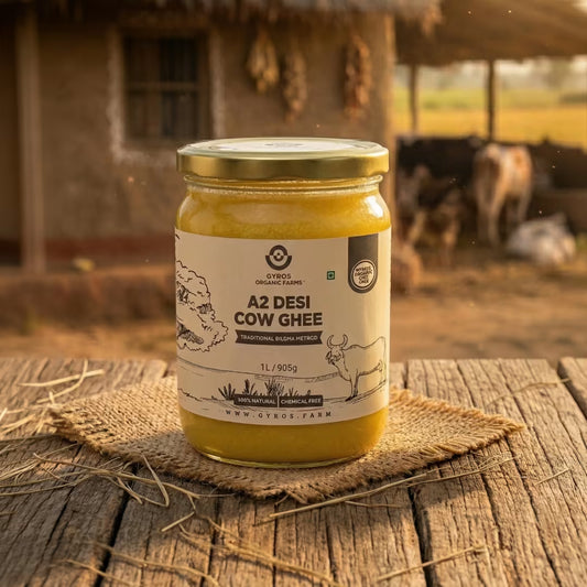 Jar of Gyros Organic Farms A2 desi cow ghee placed on a wooden surface in a rural farm setting with cows in the background.