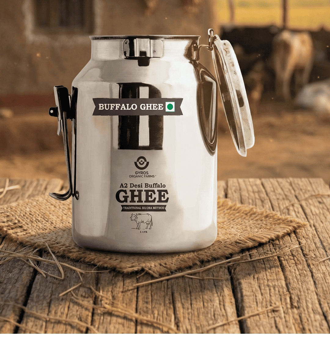 Gyros A2 desi buffalo ghee stored in a traditional steel dolchi on a wooden surface in a village setting.